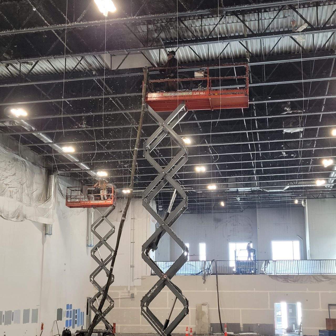 Two scissor lifts supporting overhead work inside a large commercial interior