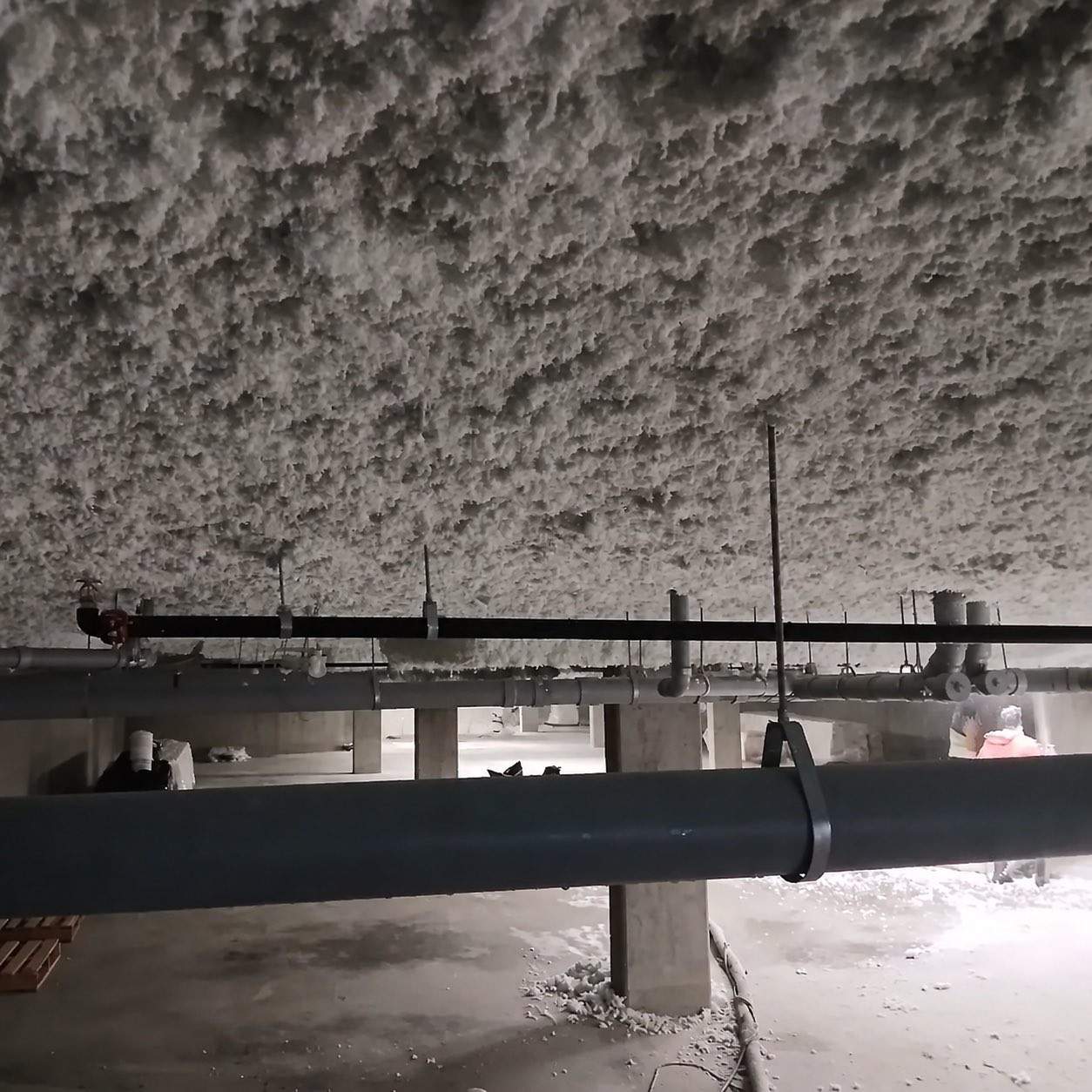 White-grey fibrous overhead insulation above pipework